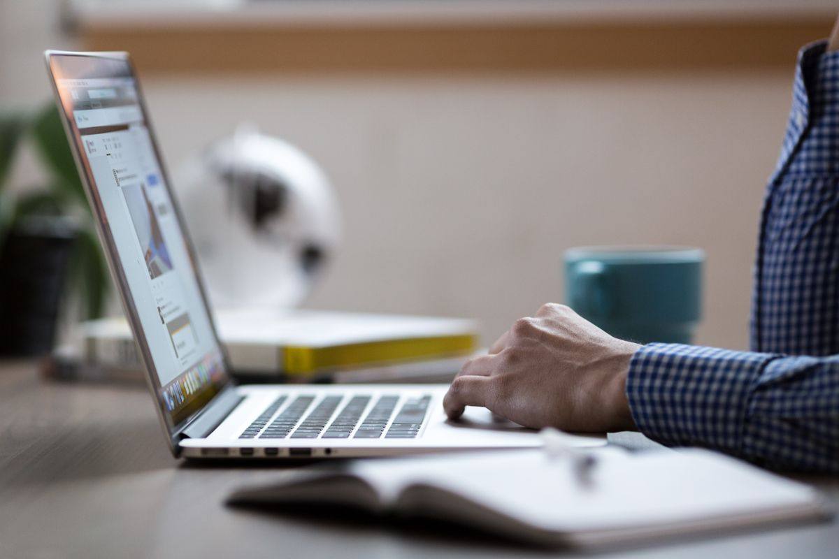 Person working on a laptop beside an open notebook and coffee mug.