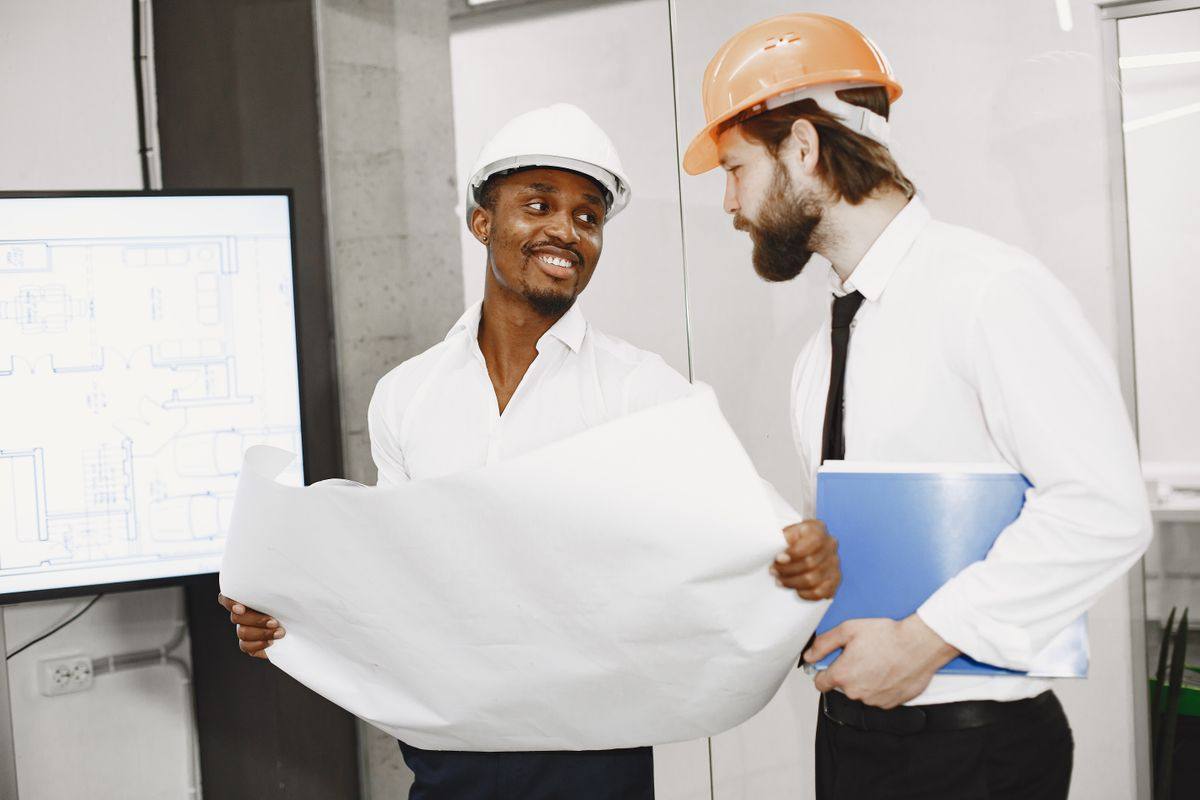 Two professionals in hard hats reviewing construction plans together.